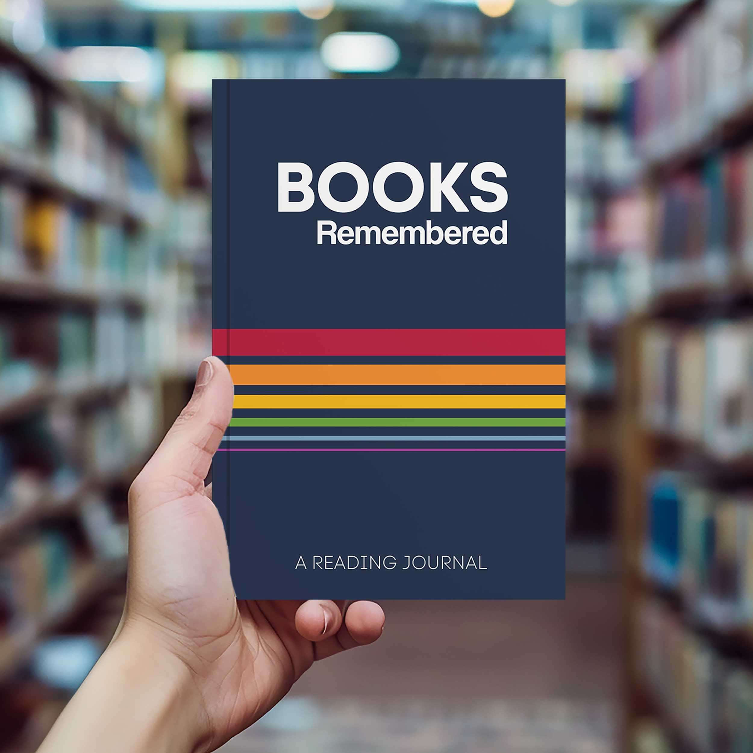 Hand holding 'Books Remembered: A Reading Journal' in a library, perfect for avid readers to track their books.