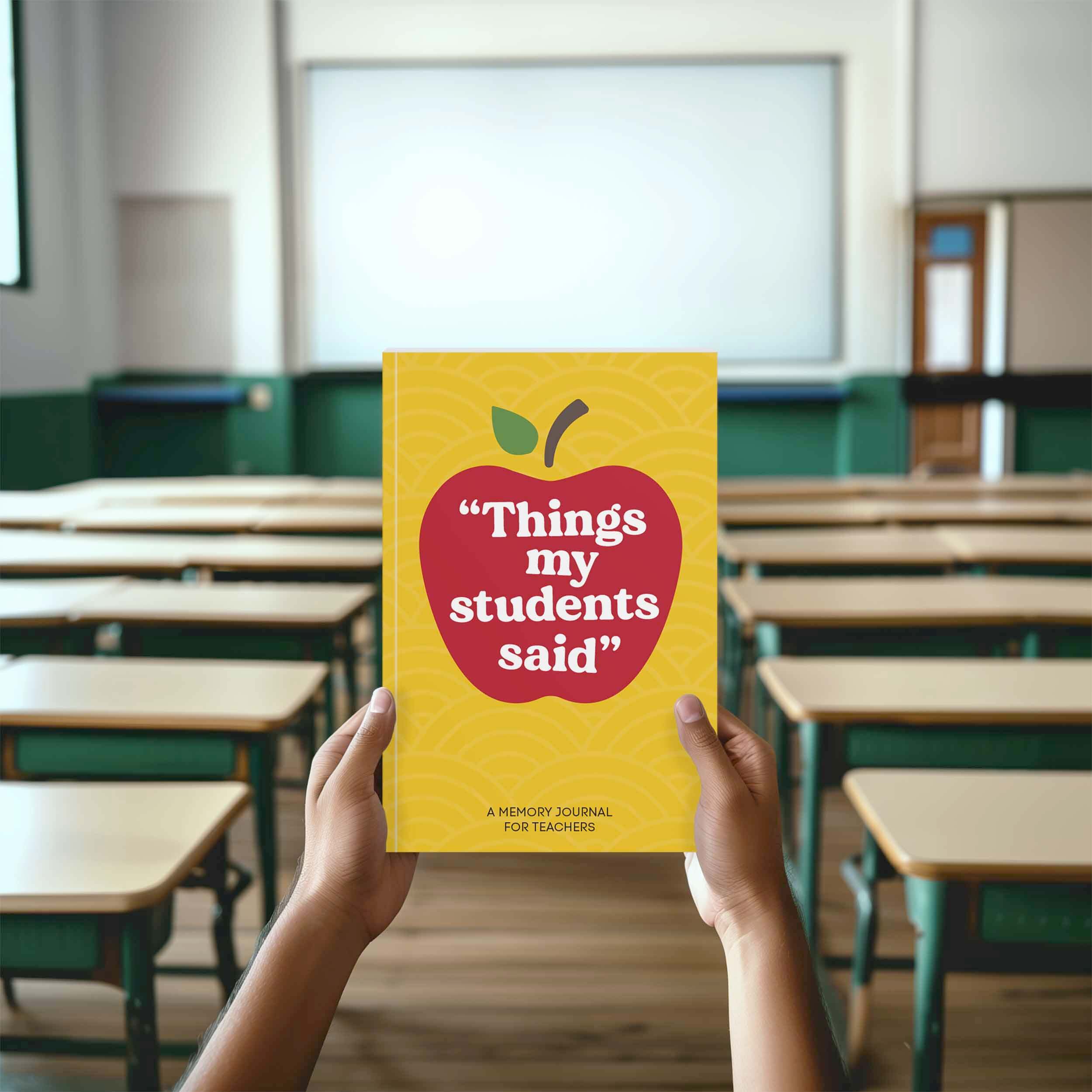 Hands holding 'Things My Students Said' quote journal in a classroom setting.