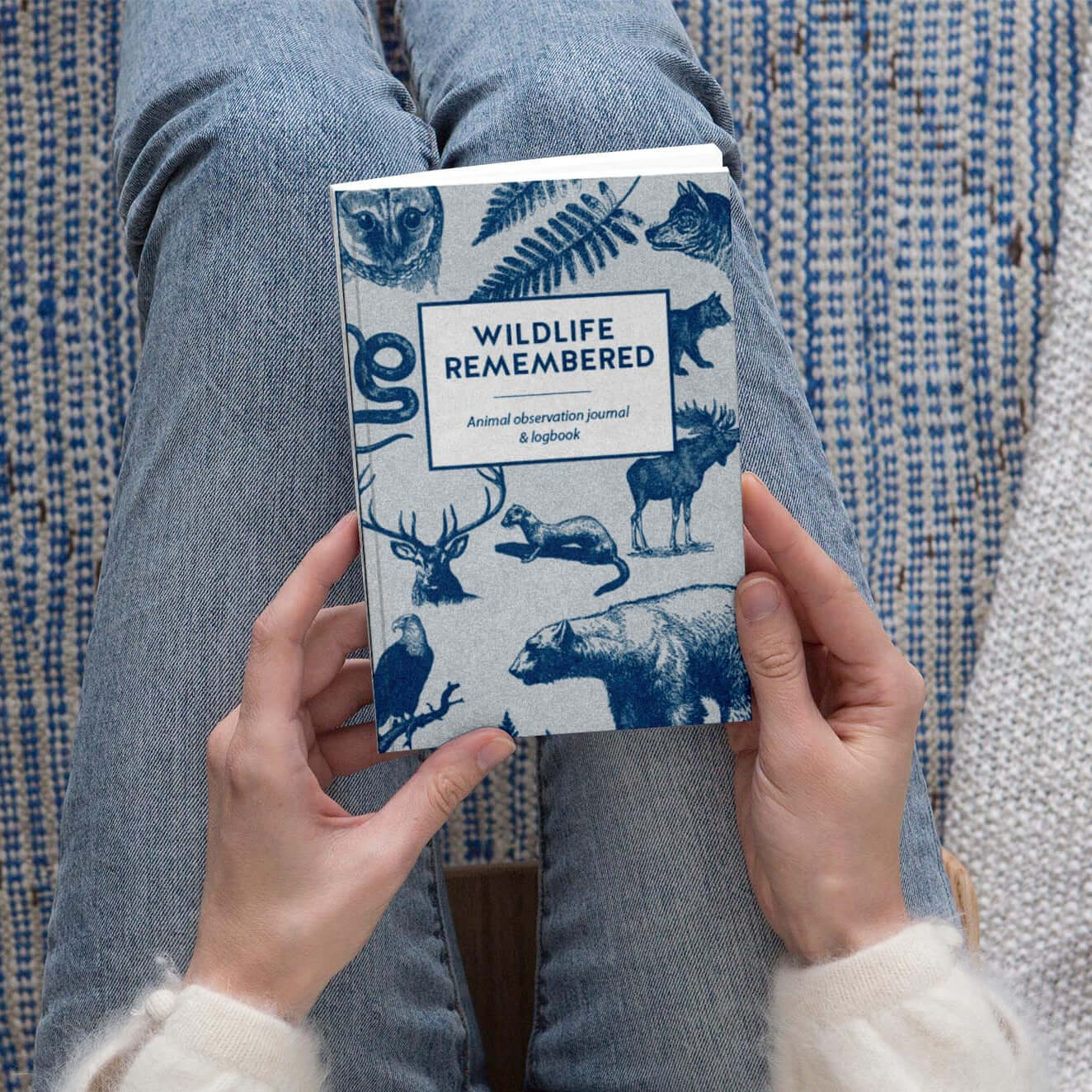 Hands holding the Wildlife Remembered animal observation journal on a cozy patterned background.